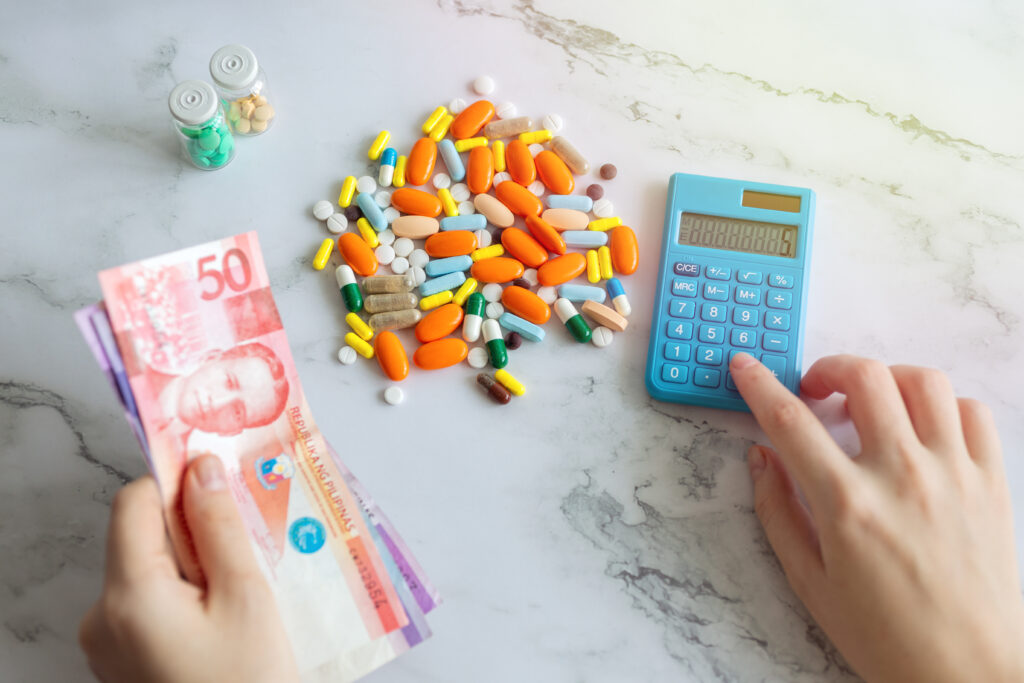 Stock photo of a person holding Philippine peso bills while calculating the costs of medicinal pills.