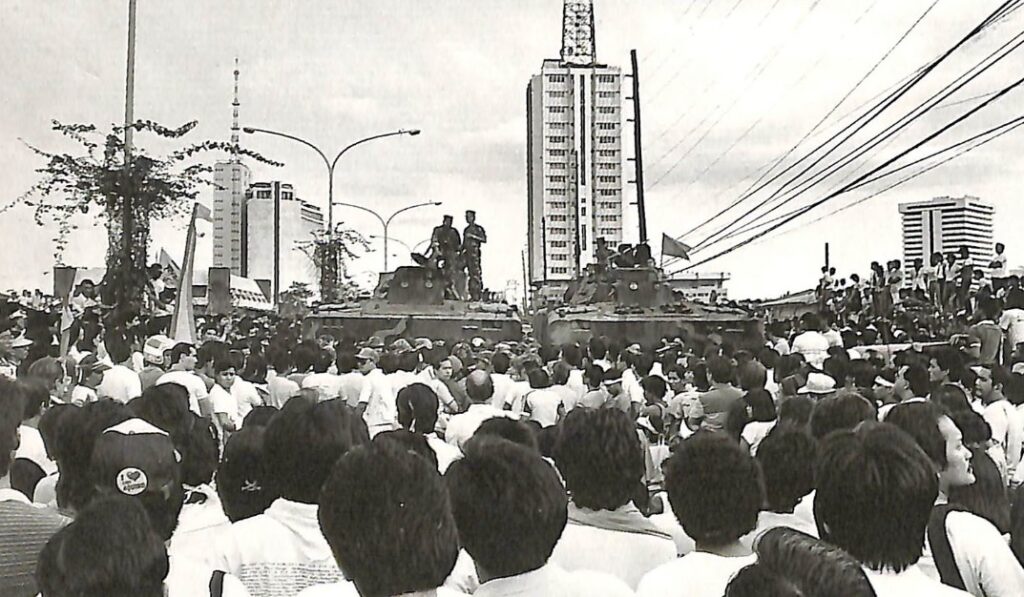 Hemmed in by thousands and unarmed men and women, the Marines keep their positions on their tanks with machine guns.