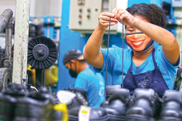A Filipino shoe factory worker wears a facemask as she produces a pair of shoes.